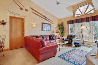 The living room at The Charter D4205 features a comfortable red leather sofa, a unique accent window, and charming ski-themed decor.