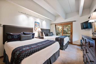 A hotel room with two twin beds, a dresser, and a television.