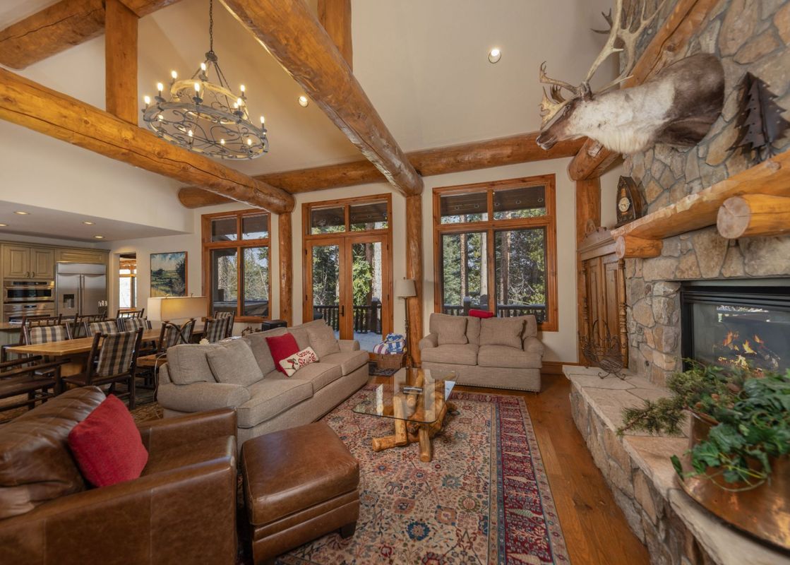 The Beavers Lodge at River Ridge features an expansive great room with a stone fireplace, antler decor, comfortable seating, and an open-concept kitchen and dining area.