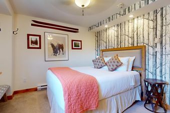 A cozy bedroom at Vantage Point 301 featuring a plush bed with coral throw, birch tree wallpaper, and rustic ski decor.