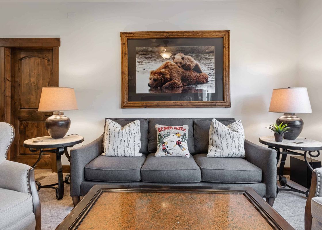 A cozy living room at The Charter D3205 with a gray sofa, decorative pillows, elegant lamps, and a large framed artwork of bears.
