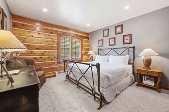 A cozy bedroom with a large bed, wooden furniture, and a mix of wood-paneled and painted walls.