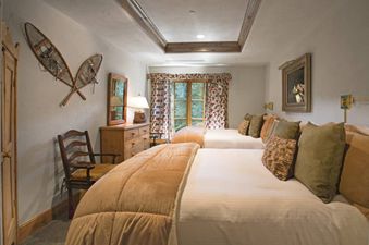 The Chateau Beaver Creek Residence 206 offers a cozy bedroom with two beds, rustic wooden furniture, snowshoes on the wall, and a window with patterned curtains.