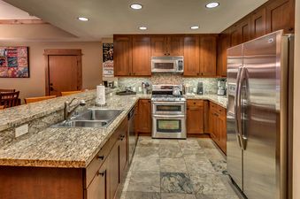 A modern kitchen with stainless steel appliances, a large double-door refrigerator, granite countertops and cherry wood cabinets.