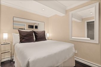 An elegantly furnished bedroom at North of Nell Unit 2D featuring a queen bed with white linens, dark brown pillows, two mirrors, and modern lighting against warm-toned walls.