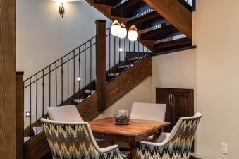 The dining area at 7 Renegade Rd Moonlight Basin Lodging has a table and four chairs, a view of the staircase, and a decorative bowl on the table.