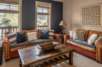 A cozy living room at Crail Creek 85 with leather sofas, a wooden coffee table, and large windows overlooking a scenic outdoor view.