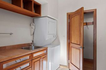 A functional laundry area at the Jay Chalet featuring a stacked washer and dryer, a wooden counter with a sink, and open wooden shelving.