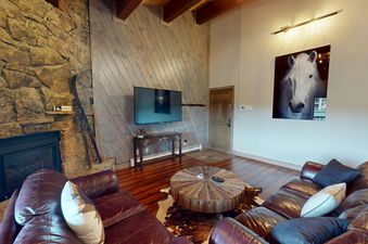 A cozy living room at Phoenix 226, featuring a stone fireplace, comfortable leather sofas, a unique round wooden coffee table, and a large flat-screen TV.