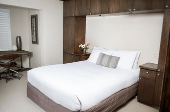 A cozy bedroom at Landmark 705, featuring a comfortable bed with white linens, a bedside table with fresh flowers, and a small desk area.