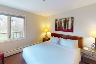 Bedroom in Manor Vail 272 with a king size bed, a nightstand with a lamp, and a window with a view of the mountains.