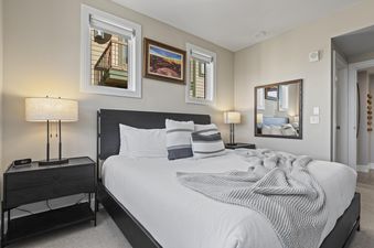 The inviting bedroom of Rio Grande 301 features a bed with white linens, grey and white striped pillows, and a textured throw blanket, flanked by black nightstands with lamps.