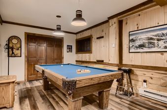 A spacious games room features a classic wooden billiard table with a bright blue felt top, set against rustic wooden walls and flooring.