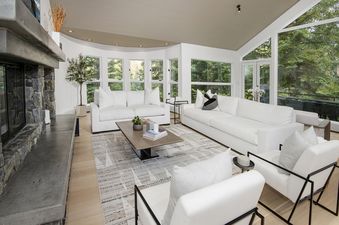 A spacious and bright living room at Rockledge 325 with white furniture, a stone fireplace, and large windows offering views of nature.