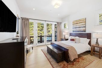 Bright bedroom with a dark wood bed and glass French doors leading to a balcony at Snow Dance at The Colony.