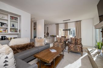 A living room with a large sectional sofa, a coffee table, and two armchairs in front of a large window overlooking a snowy mountain view.