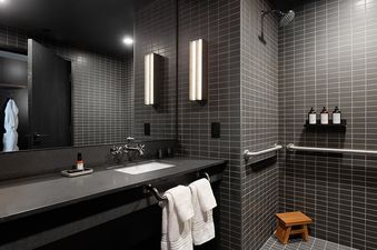 A modern bathroom featuring dark grey subway tiles, a sleek vanity with a large mirror, and an accessible shower with grab bars and a rain shower head.