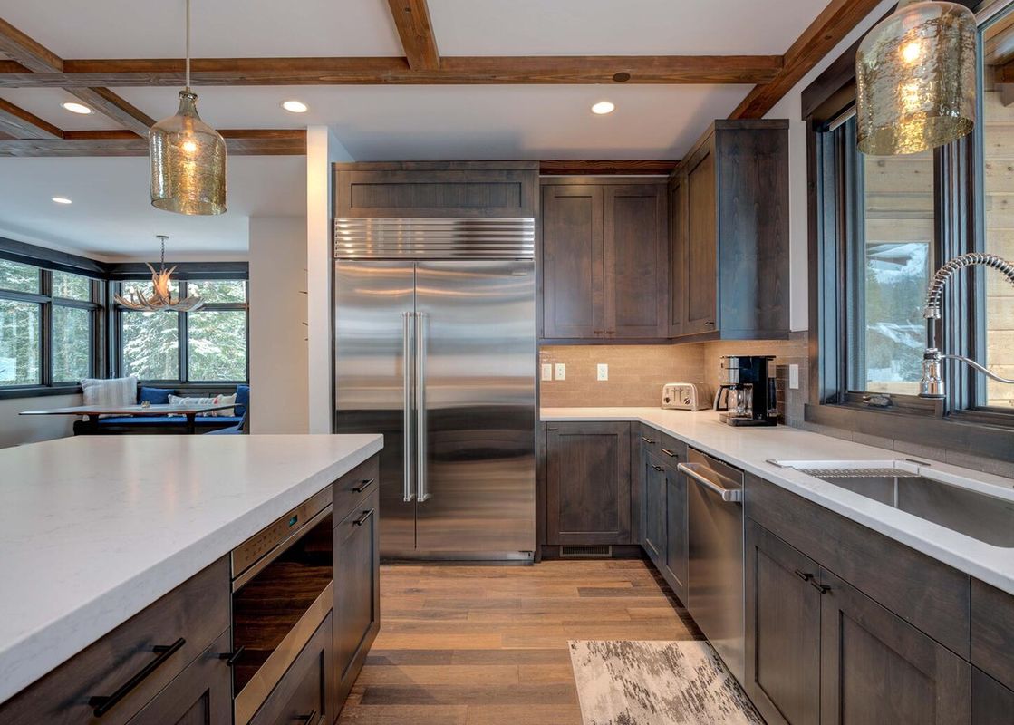 The kitchen of Moonlight Basin 6 Jakes Lane is well equipped with stainless steel appliances, a double door fridge, oven, dishwasher and a large white quartz countertop. The kitchen has dark wood cabinets and hardwood floors.