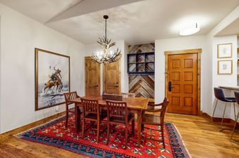 A dining room with a wooden table and chairs, a rug, and a chandelier