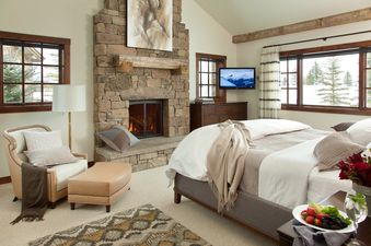 Cozy master bedroom with a stone fireplace and snow-covered views outside the windows.