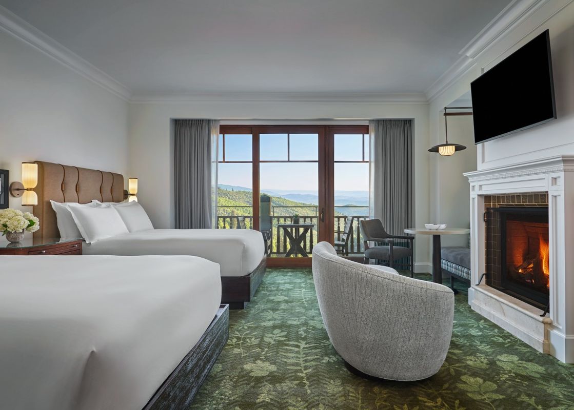 A hotel room with two queen beds, a fireplace, and a balcony with a mountain view.