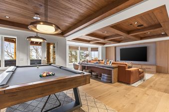 A luxurious entertainment area featuring a billiard table, a comfortable living area with a large TV, and expansive windows offering outdoor views.