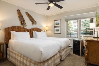 A cozy bedroom at Montaneros 412 with two beds, each featuring white linens and checkered bed skirts, complemented by rustic snowshoe decor and a ceiling fan.