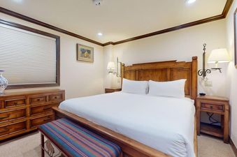 A bedroom in Vantage Point 401 features a wooden bed frame with white linens, complemented by wooden furniture and a colorful bench.