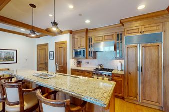 A kitchen with a granite countertop and a breakfast bar, a stainless steel stovetop, and a refrigerator with a wooden panel door.