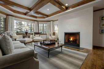 A luxurious living room in Chateau Beaver Creek Residence 1403 with a roaring fireplace, large windows showcasing a snowy view, comfortable seating, and exposed wooden ceiling beams.
