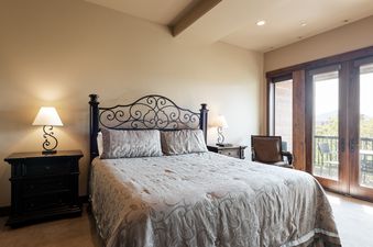 A primary bedroom at 103 Juniper Landing with a wrought iron bed, two nightstands with lamps, a brown leather armchair, and a balcony with an outdoor view.