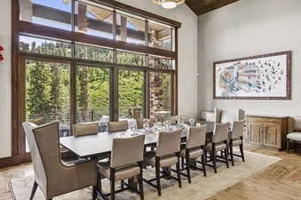 An elegant dining area at Grandview at The Colony featuring a large wooden table and tall windows with scenic forest views.