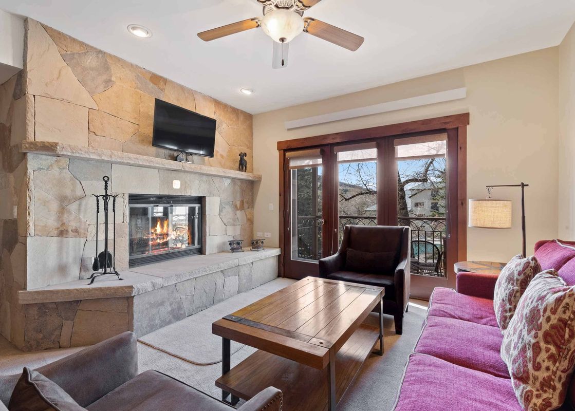 A cozy living room at The Charter C1405 with a stone fireplace, magenta sofa, and wooden coffee table.