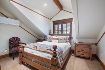 A cozy bedroom at Timber Lodge at the Oaks with a queen-sized wooden bed, southwestern-patterned bedding, a unique armchair, and a wall-mounted air conditioning unit.