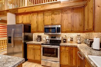 A fully equipped kitchen with wooden cabinetry, granite countertops, and stainless steel appliances at Moosehead Cabin.