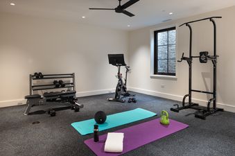 A well-equipped fitness room at Northern Hideaway features a Peloton bike, free weights, a power tower, and yoga mats on a dark speckled floor.