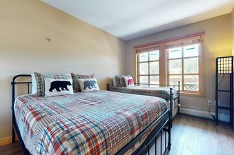 A bedroom with two beds, a plaid comforter, and bear-themed pillows.