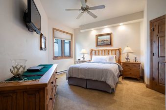 The bedroom at Chateau Chamonix CX311, featuring a rustic wooden bed, matching nightstands, a wall-mounted TV, and a dresser.