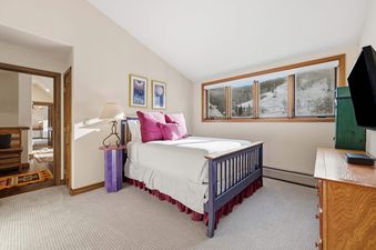 A cozy bedroom with a blue-framed bed, fuchsia pillows, and large windows offering a snowy mountain view.
