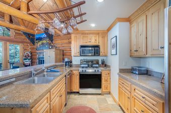 A modern rustic kitchen in Summit Cabin See Forever Cabin 103 with light wood cabinets, granite countertops, and stainless steel appliances.