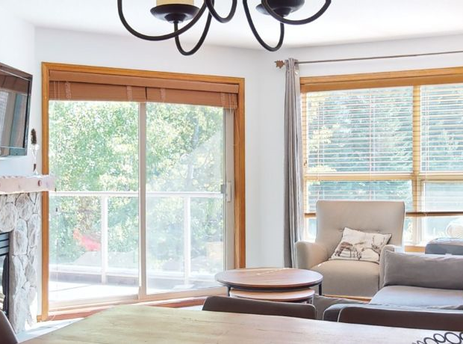 The living area within Aspens on Blackcomb Unit 332 features a cozy fireplace, comfortable seating, and a large window that offers views of the lush green outdoors.