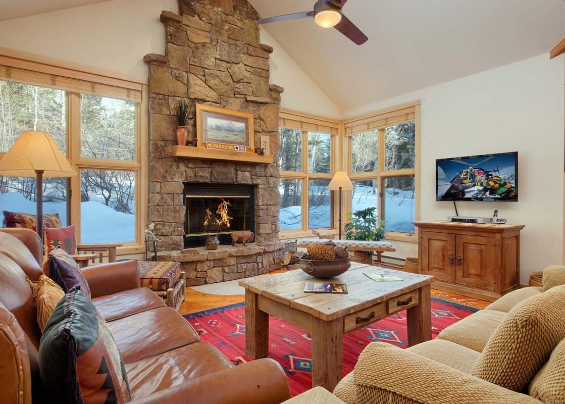 Cozy living room with stone fireplace, comfortable sofas, and winter views outside at Moose Creek 14.
