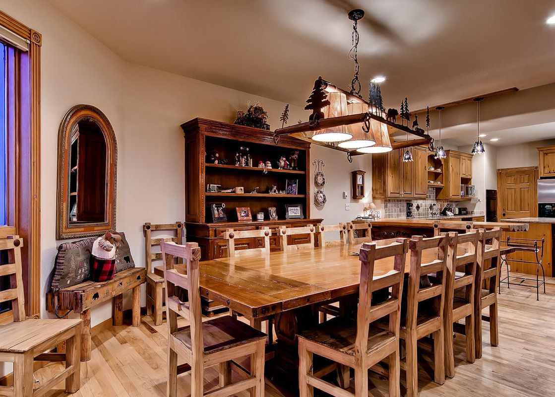A rustic dining area with a long wooden table and chairs, a large hutch, and a kitchen area in the background at His High Place.