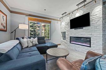 A cozy lounge area in The Charter E0205 with a blue sectional sofa, a round coffee table, and a fireplace with a mounted TV.