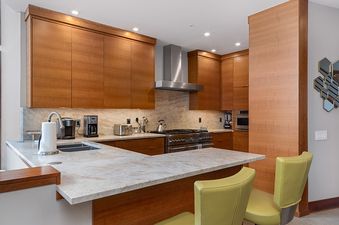 A modern kitchen with stainless steel appliances, wood cabinets, and a large island with seating.