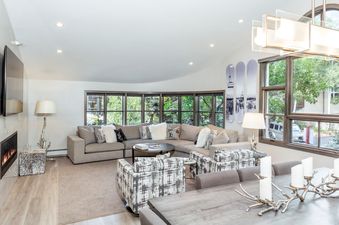 The luxurious living area of Vail Center Place 3 Bedroom Diamond Unit 3 features a large sectional sofa, two armchairs, a fireplace, and views of the lush greenery outside.