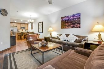 A spacious, open-concept living room at BlueSky Breckenridge 410 features brown leather and suede sofas, a wooden coffee table, and an antler-base lamp.