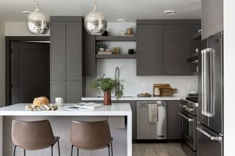 A modern kitchen in Penthouse on Glenwood 401 with dark wood cabinets, white quartz countertops, stainless steel appliances, and a kitchen island with two leather bar stools.