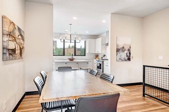 The dining area and kitchen of the Luxury Alpine Abode are showcased, featuring a large wooden dining table with black chairs and a modern kitchen with white cabinetry and stainless steel appliances.