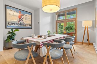 A modern dining table with six chairs set next to a glass door looking out onto a green forest in Moose Creek 15.